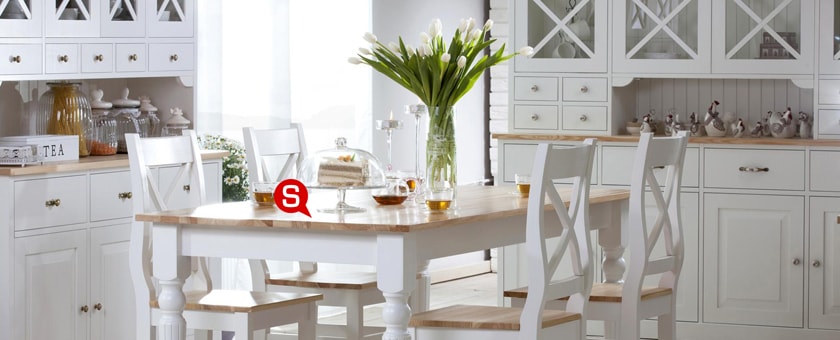 Jadalnia w stylu prowansalskim z pięknym drewnianym stołem, na którym stoi wazon z tulipanami. Białe krzesła dopasowane do całej aranżacji dodają charakteru wnętrzu.
